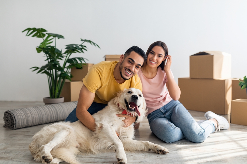 Happy young couple with their dog posing on floor of new home on moving day. ©Prostock-studio